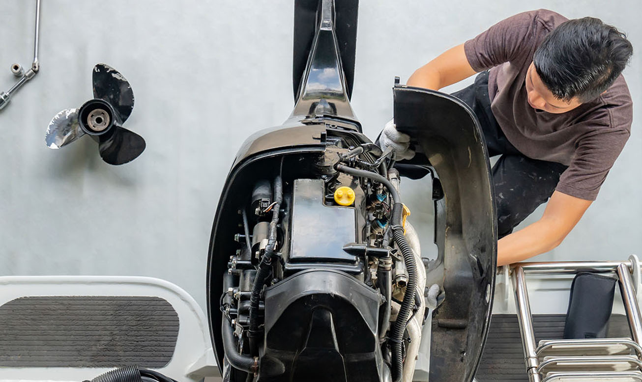 Technician performing outboard motor service on a boat